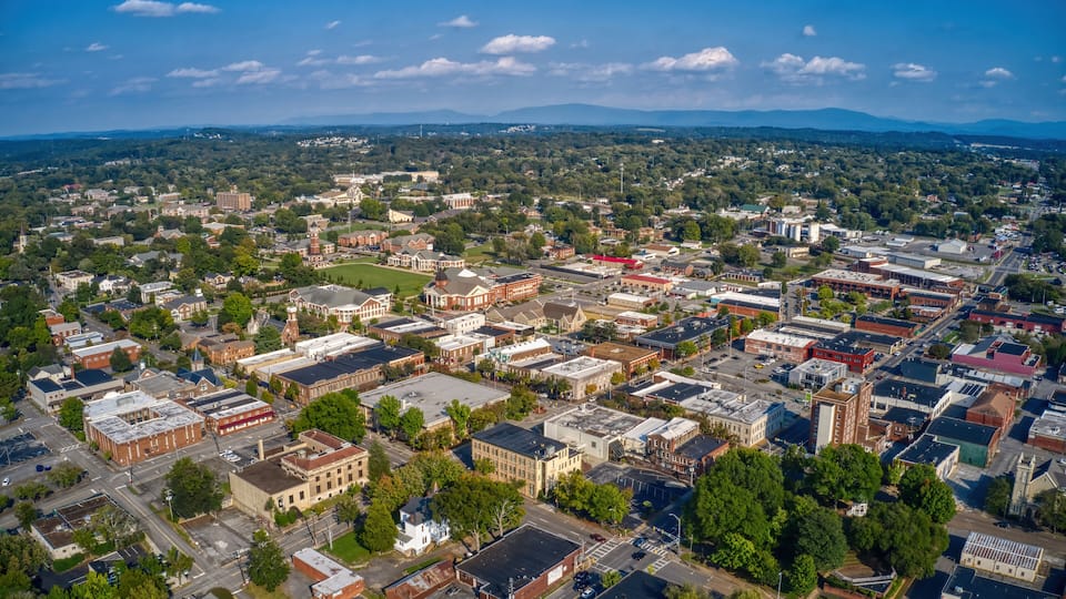 An aerial view of a town with historic buildings, a church steeple, and a river in the background.