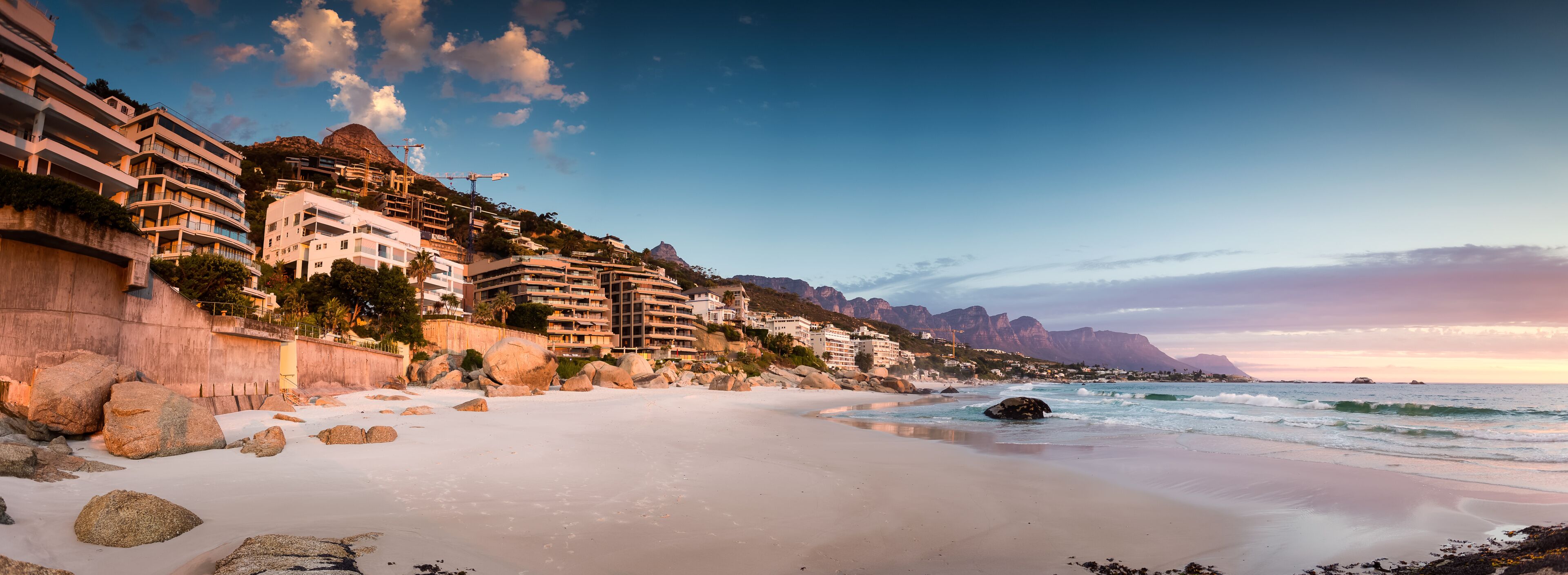 A coastal town with beachfront buildings, a sandy beach, and rocky outcrops.