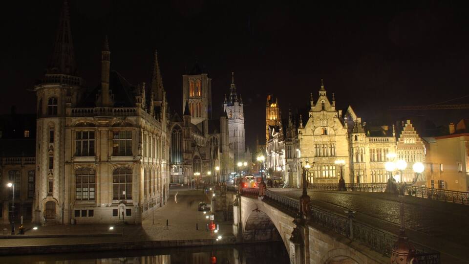 Vista nocturna de una ciudad histórica con edificios iluminados y un puente sobre un canal.