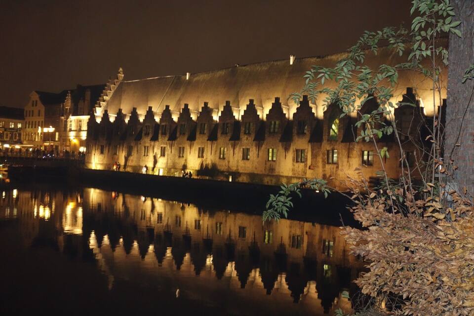 Un edificio histórico con techo de paja, reflejado en aguas tranquilas durante la noche.