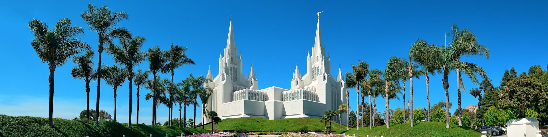 A large white church with multiple spires, surrounded by palm trees and a well-maintained garden.