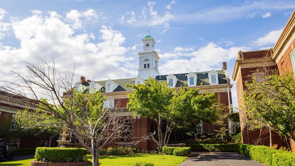 A historic building with a clock tower, surrounded by well-maintained gardens and a clear blue sky.