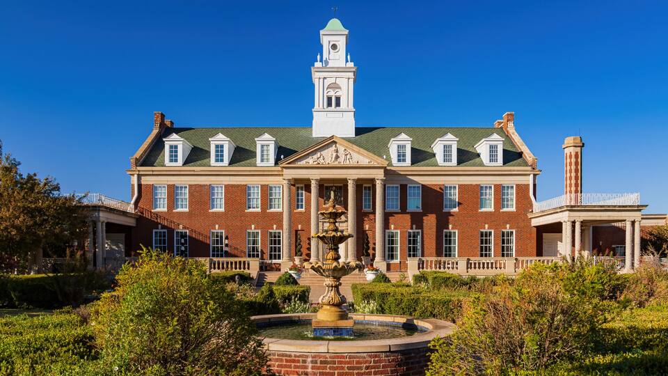A large brick building with a central fountain, a tower, and a well-maintained garden.