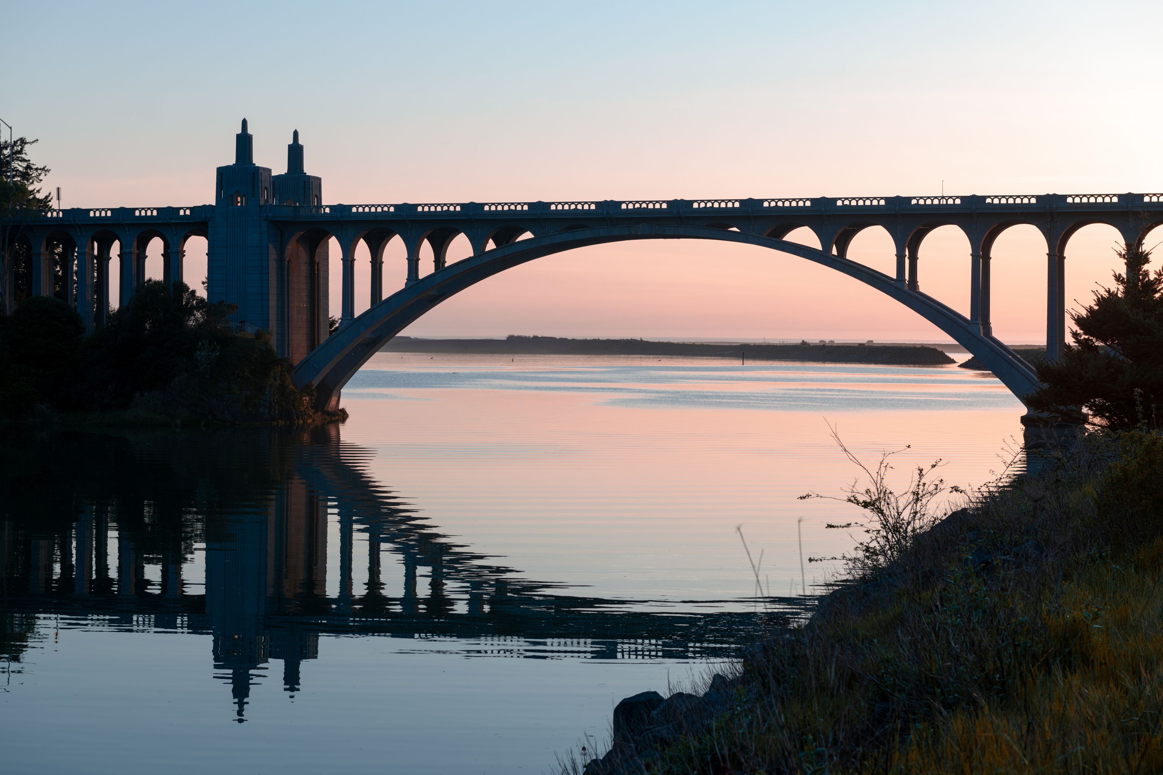 Un puente sobre aguas tranquilas con un atardecer al fondo.