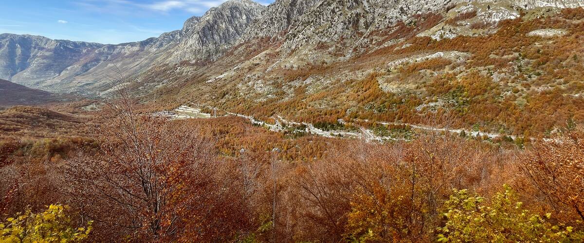 Scenic autumn view of the mountains and valley in Malësi e Madhe, northern Albania, with vibrant foliage and rugged peaks.