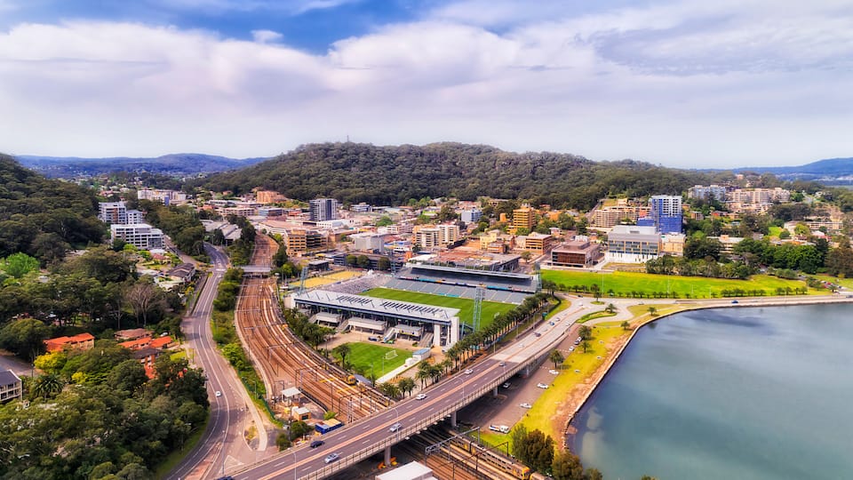 A cityscape with a river, a stadium, and a bridge.