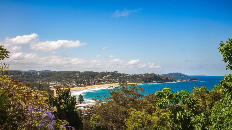 A coastal landscape with a beach, ocean, and hills.