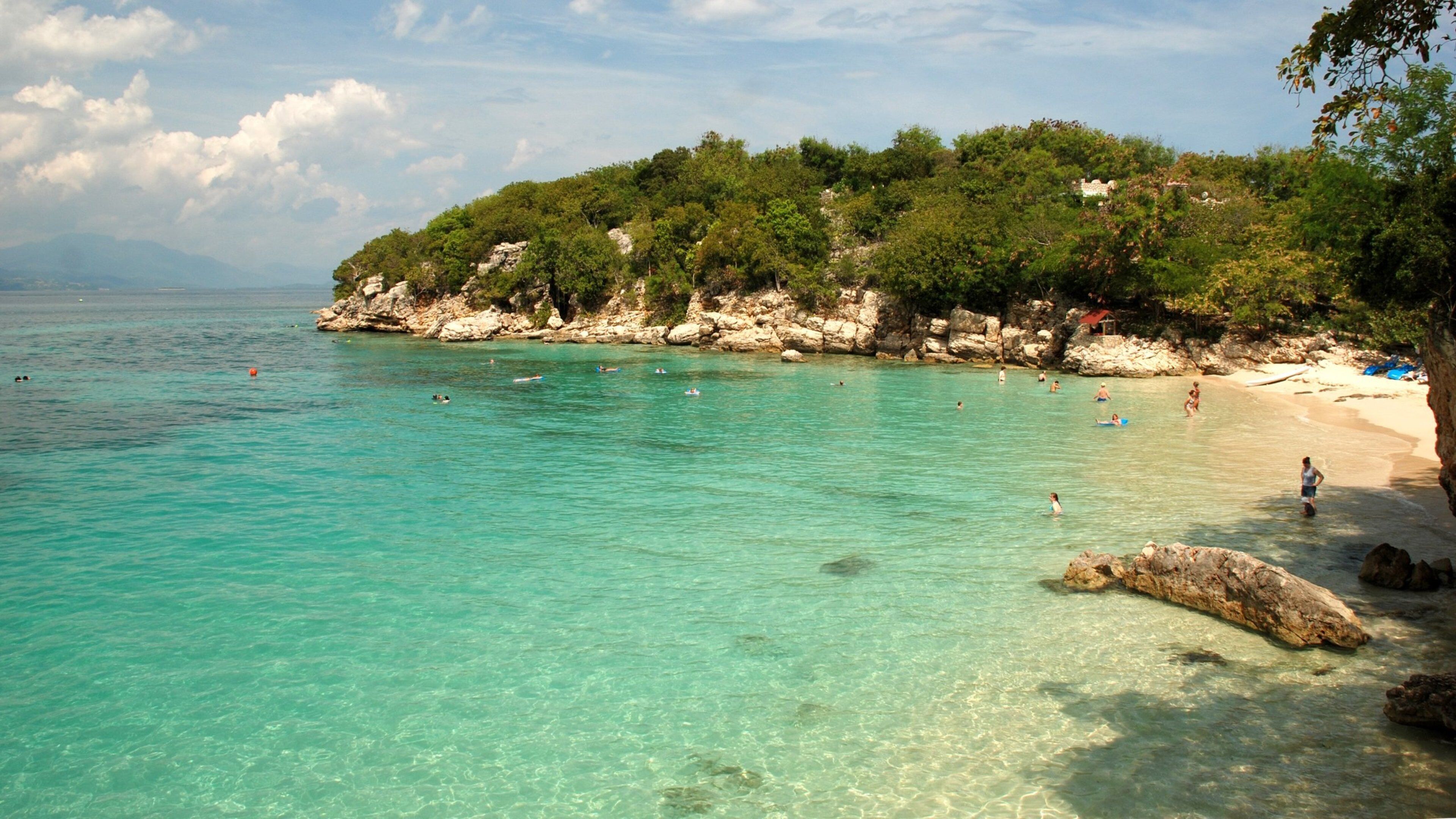 A turquoise beach with clear water, rocky cliffs, and lush greenery.