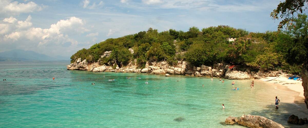 A turquoise beach with clear water, rocky cliffs, and lush greenery.