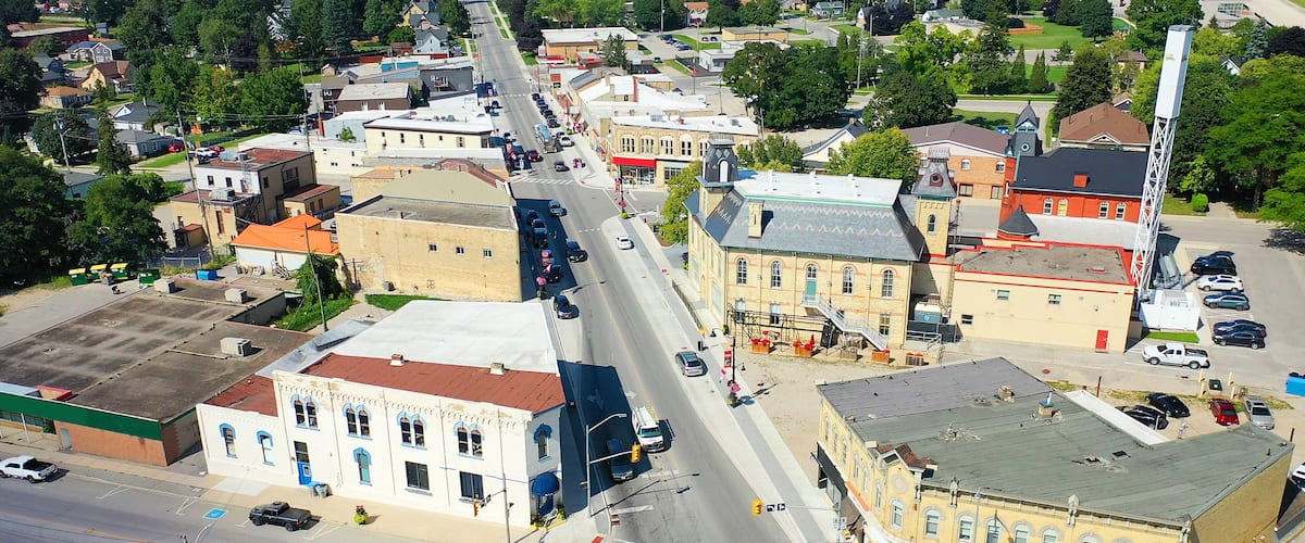 An aerial view of a small town with a main street, various buildings, and parked cars.