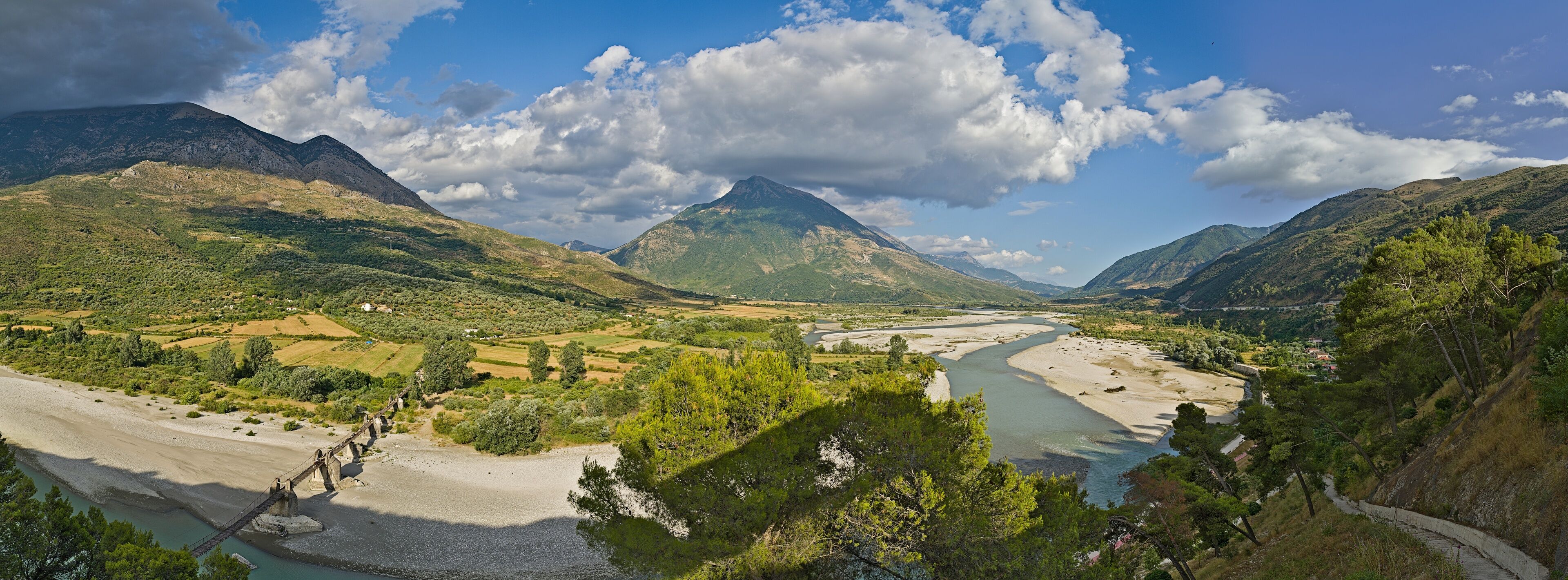 A river winding through a valley with mountains in the background and a bridge over the river.