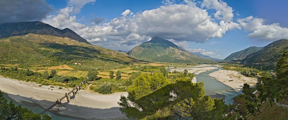 A river winding through a valley with mountains in the background and a bridge over the river.