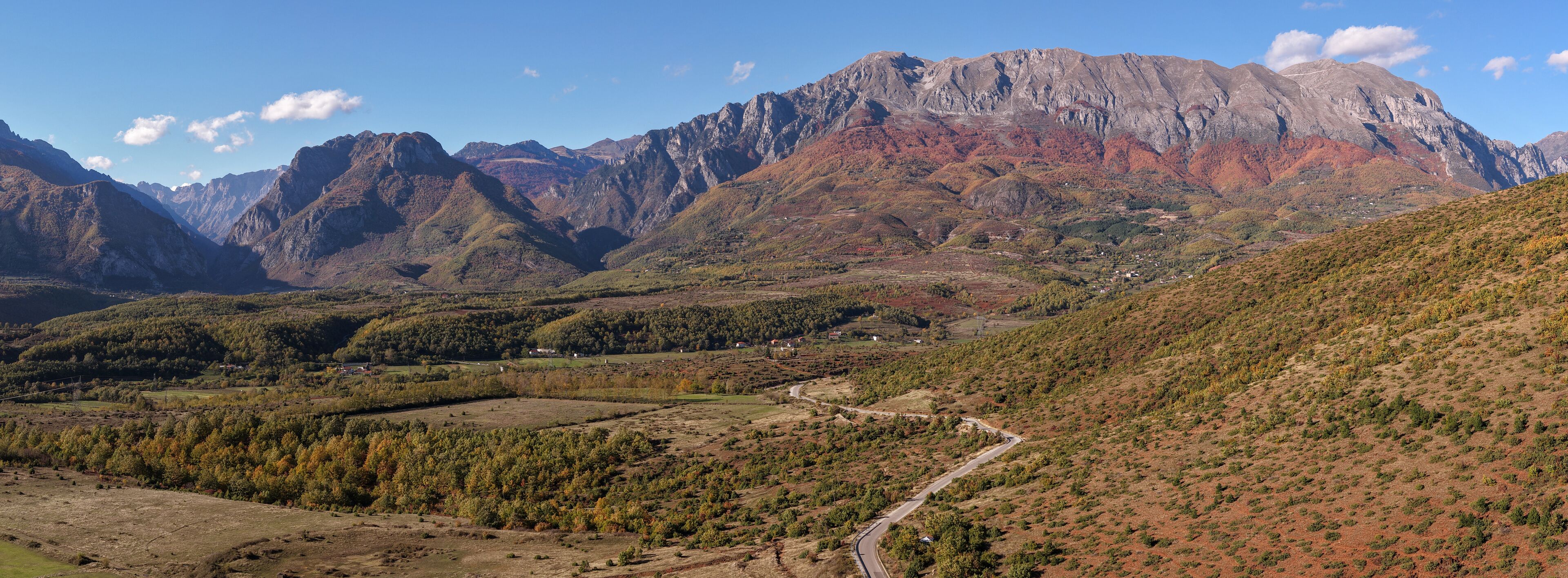 A mountainous landscape with a winding road, dense forests, and a village.