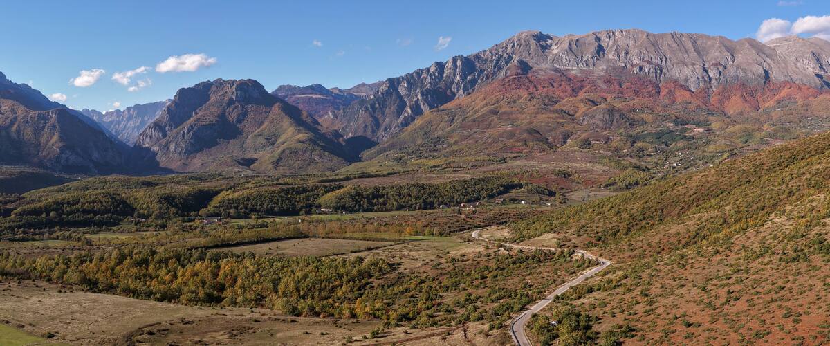 A mountainous landscape with a winding road, dense forests, and a village.