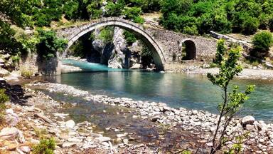 A stone bridge over a clear river surrounded by lush greenery.
