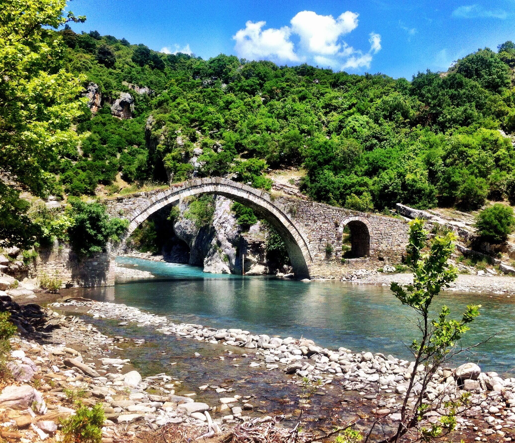 A stone bridge over a clear river surrounded by lush greenery.