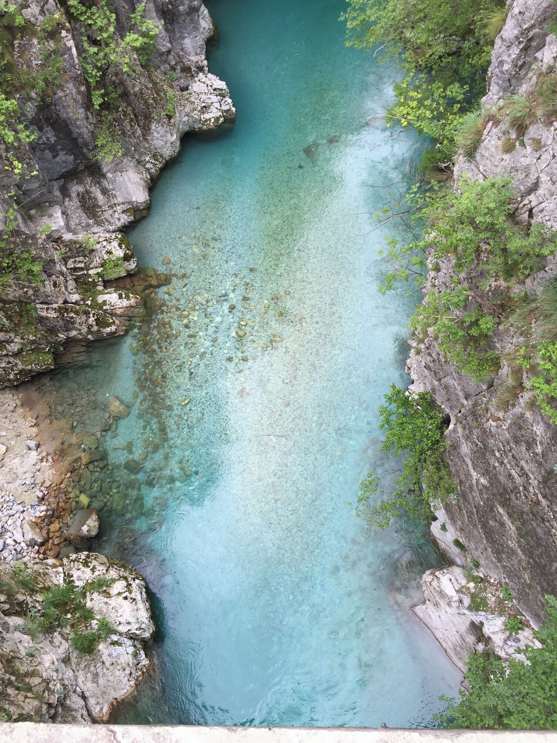 A clear turquoise river surrounded by rocky cliffs and lush greenery.