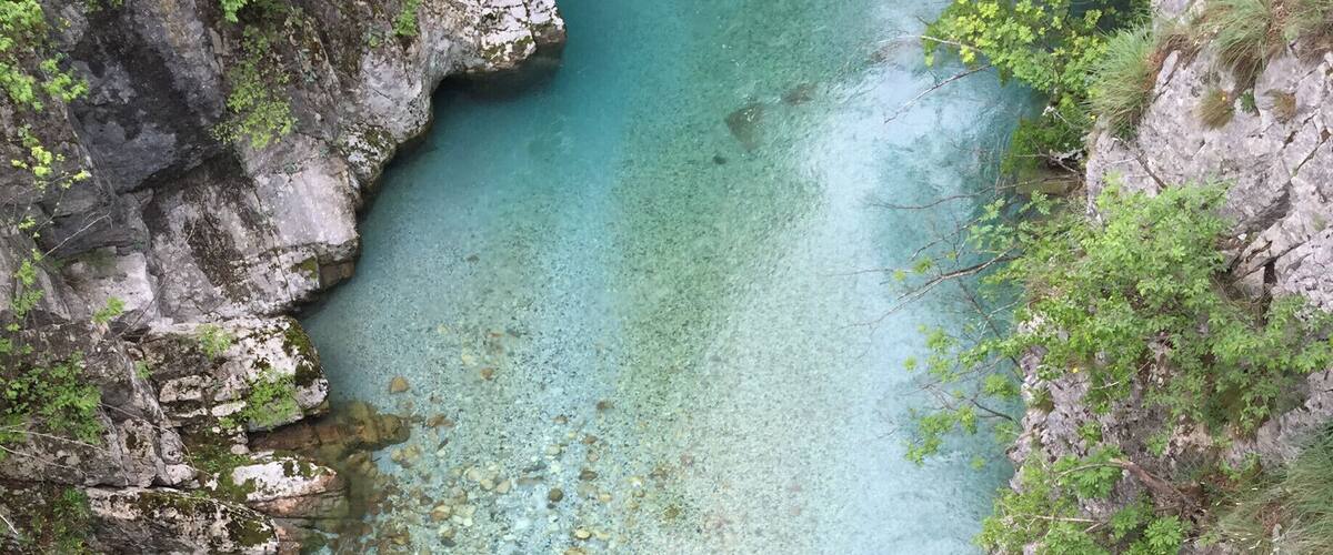A clear turquoise river surrounded by rocky cliffs and lush greenery.