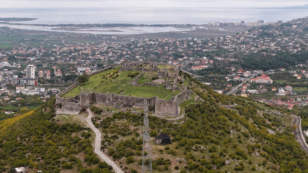 Aerial view of Lezhë Castle overlooking the city, surrounding hills, and the Adriatic coastline under a soft cloudy sky.