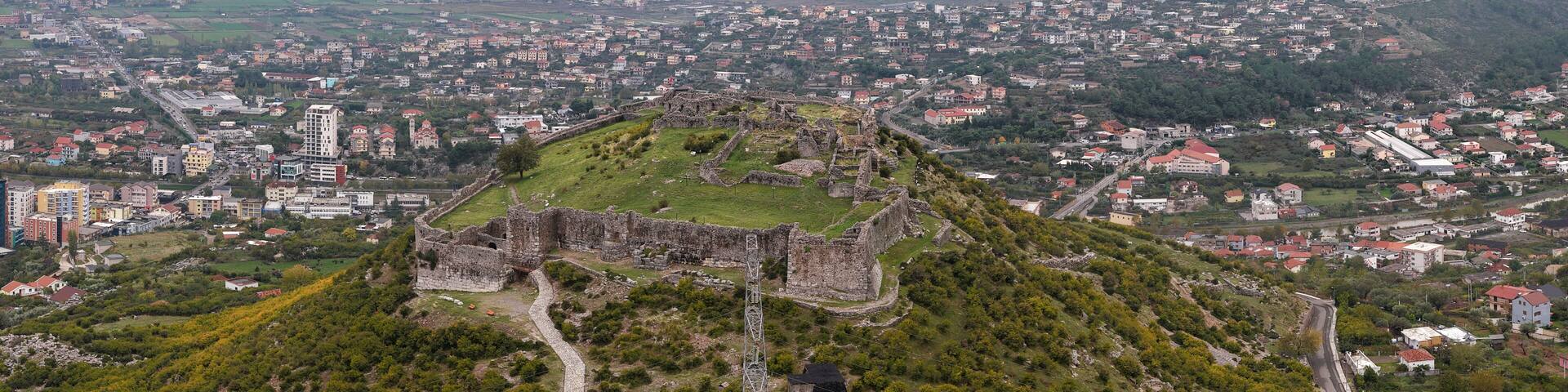 Aerial view of Lezhë Castle overlooking the city, surrounding hills, and the Adriatic coastline under a soft cloudy sky.