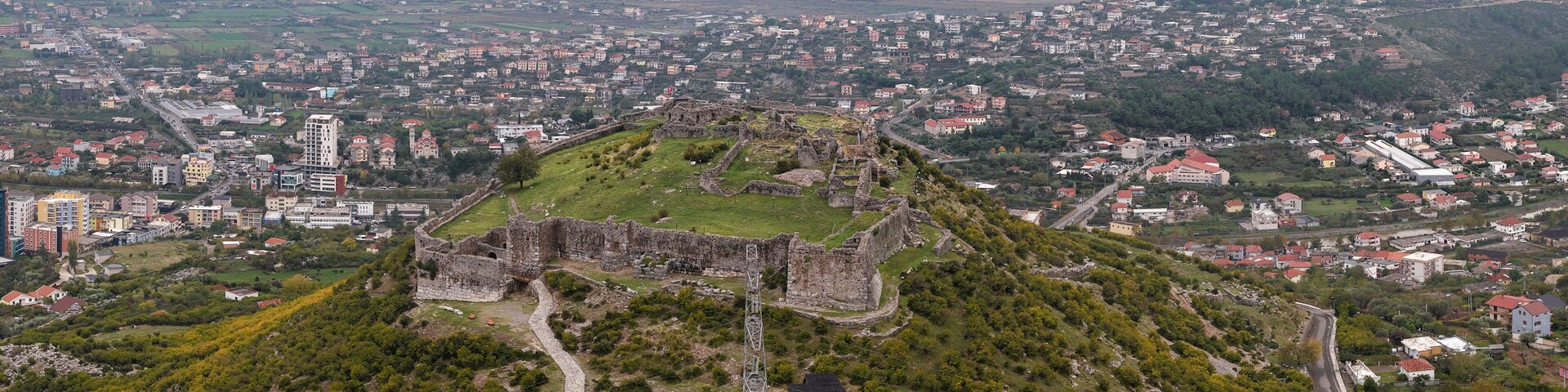 Aerial view of Lezhë Castle overlooking the city, surrounding hills, and the Adriatic coastline under a soft cloudy sky.
