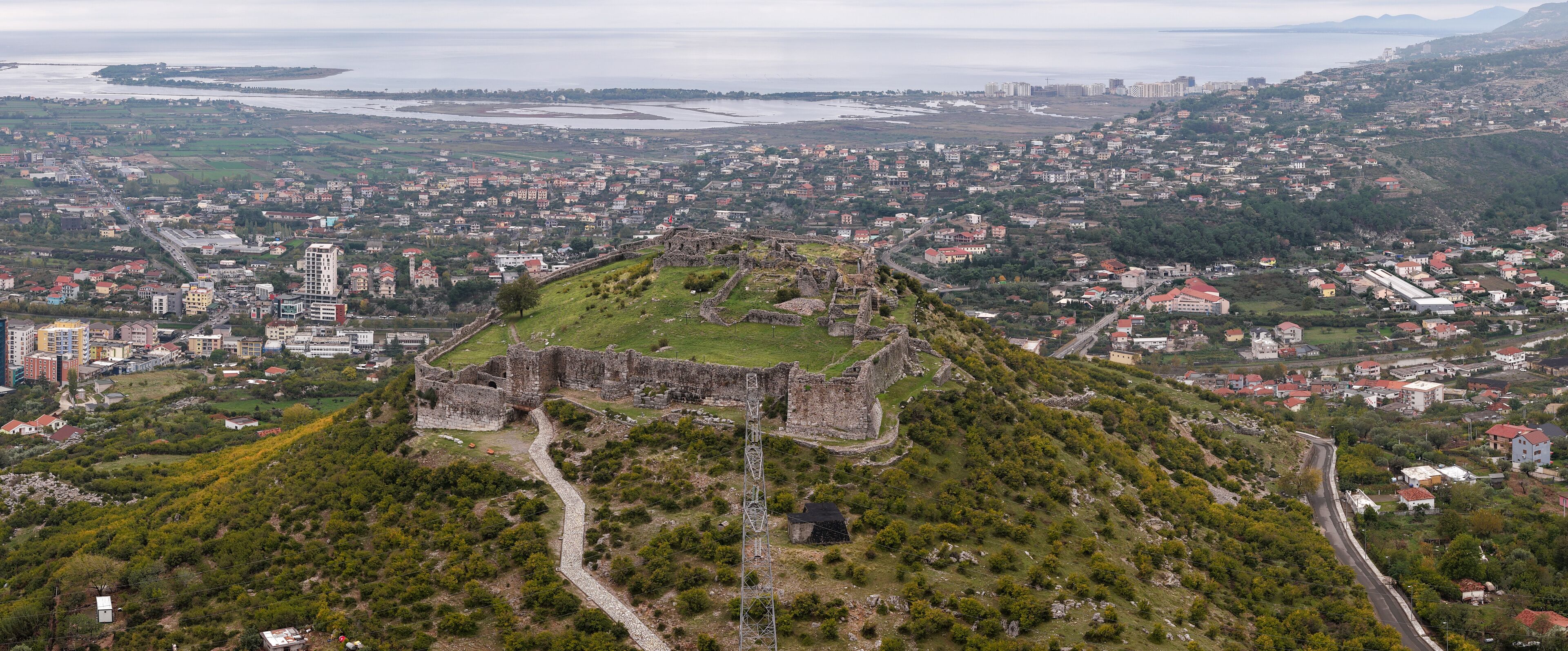 An aerial view of a historic fortress surrounded by a cityscape, with a coastal background.