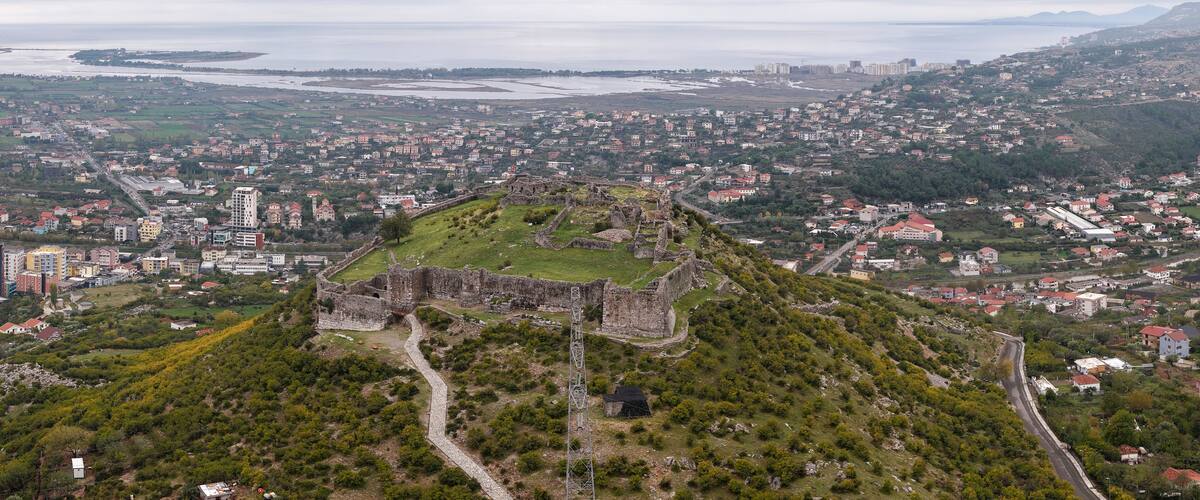 An aerial view of a historic fortress surrounded by a cityscape, with a coastal background.