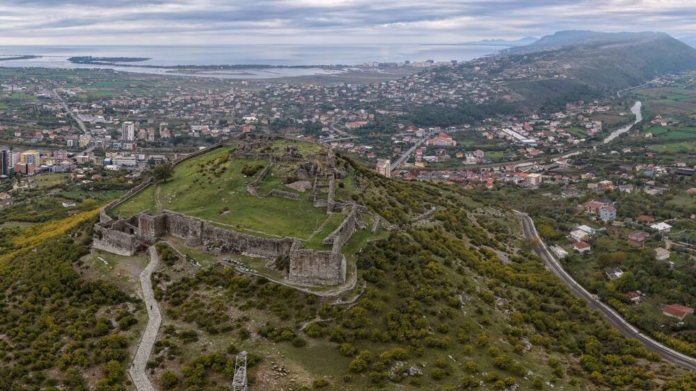 Aerial panorama of Lezhë Castle overlooking the city, Drin River and Adriatic coastline under soft cloudy light.