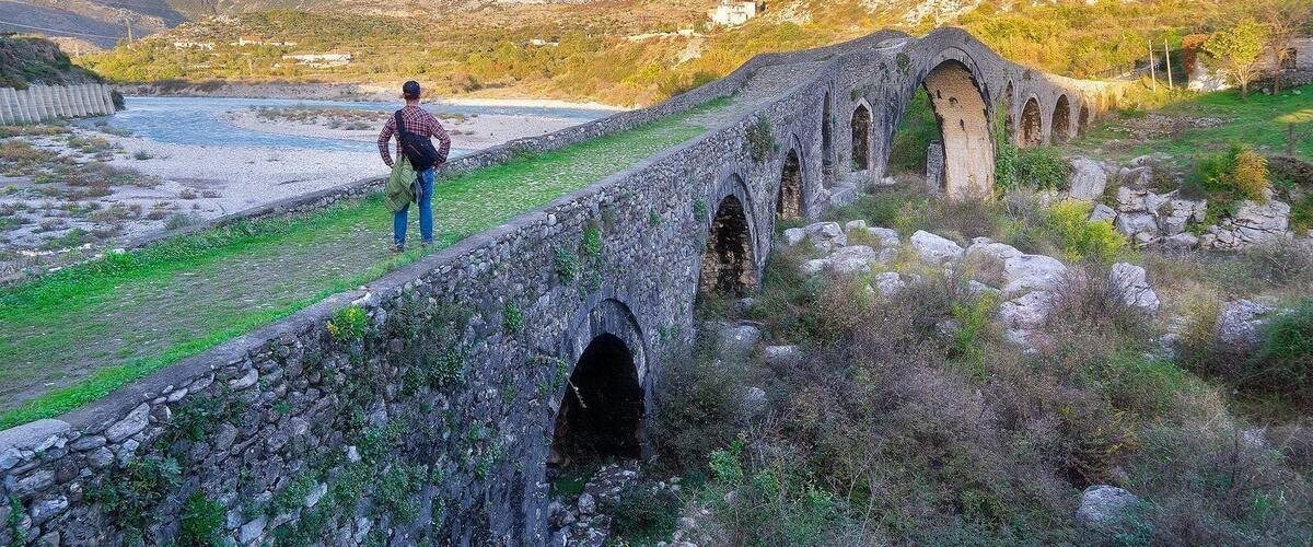 A stone bridge with arches over a river, surrounded by hills and sparse vegetation.
