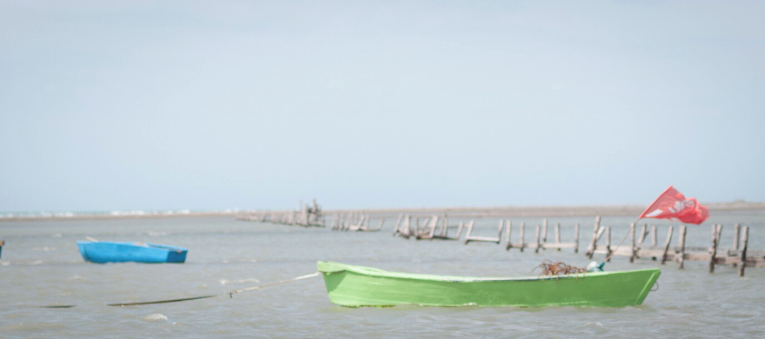 A green boat tied to a dock with a red flag on a calm body of water.