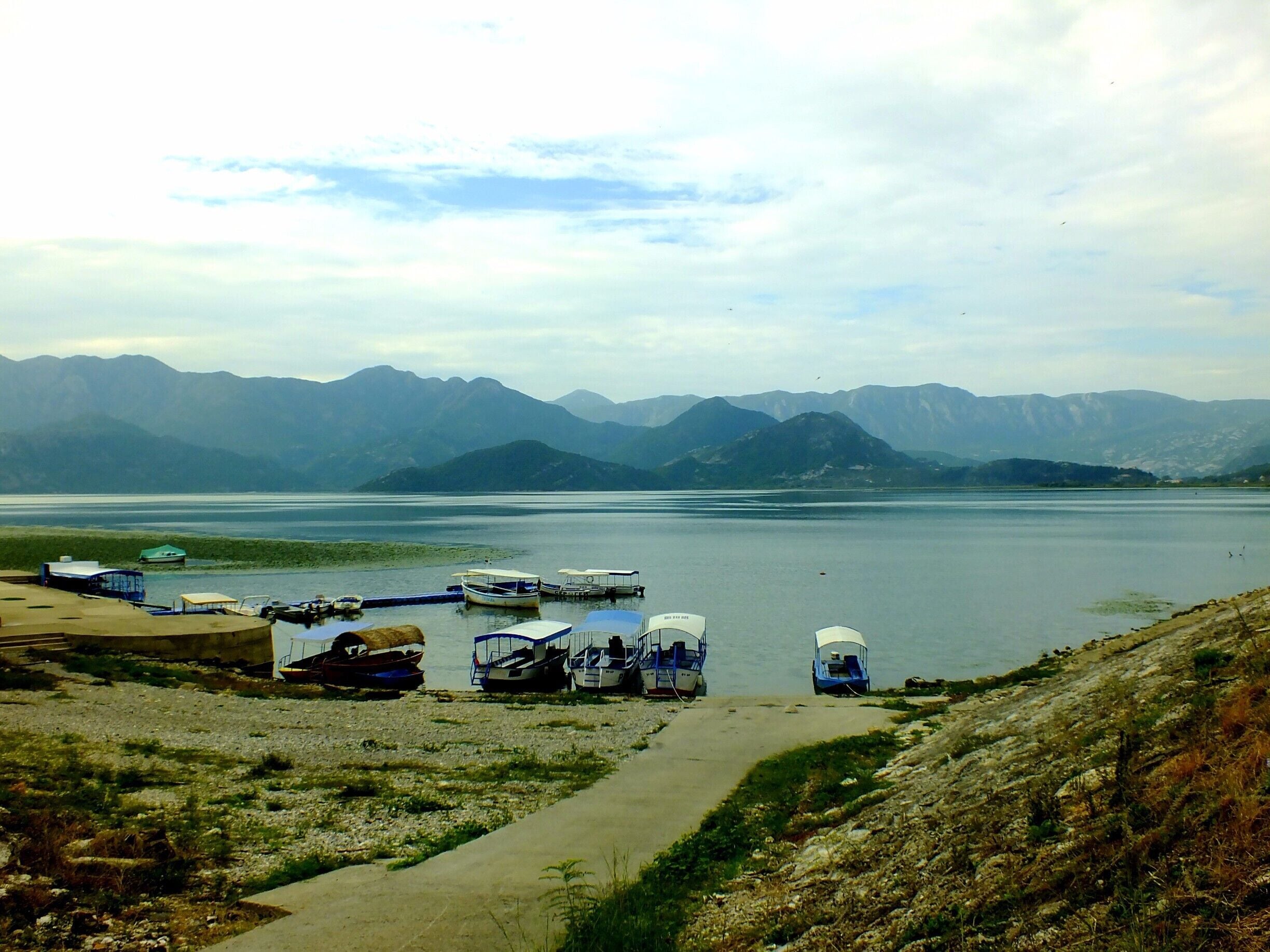 A lake with boats docked along the shore, surrounded by mountains.
