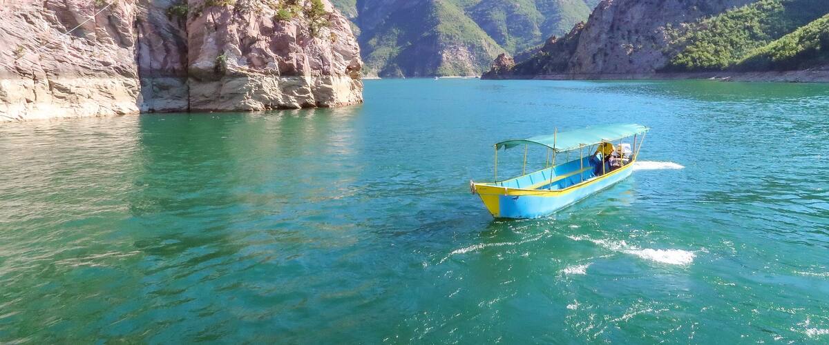 A boat on a clear turquoise lake surrounded by rocky cliffs and mountains.