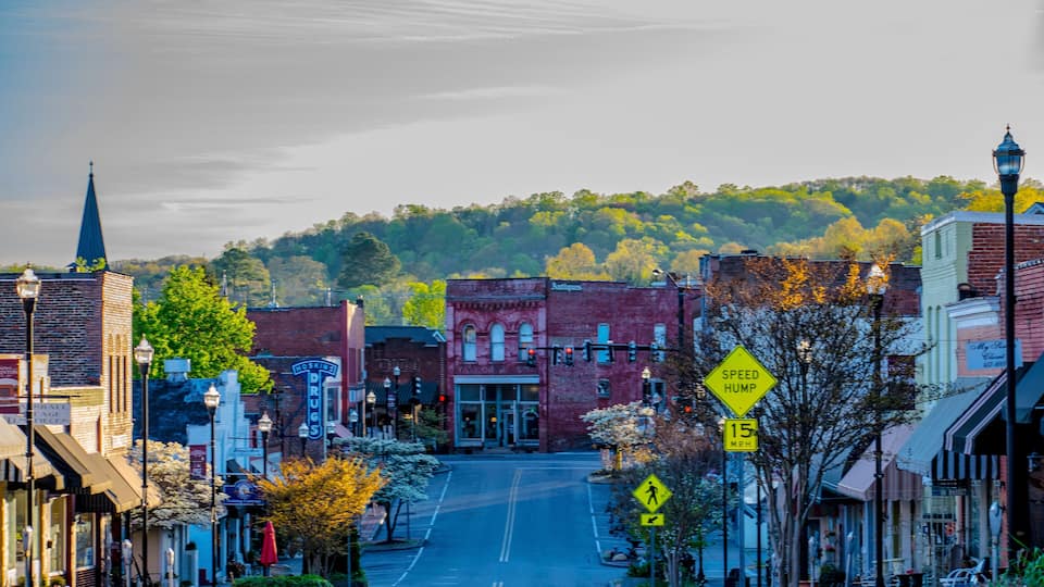 A town street with buildings, a church spire, and a speed hump.