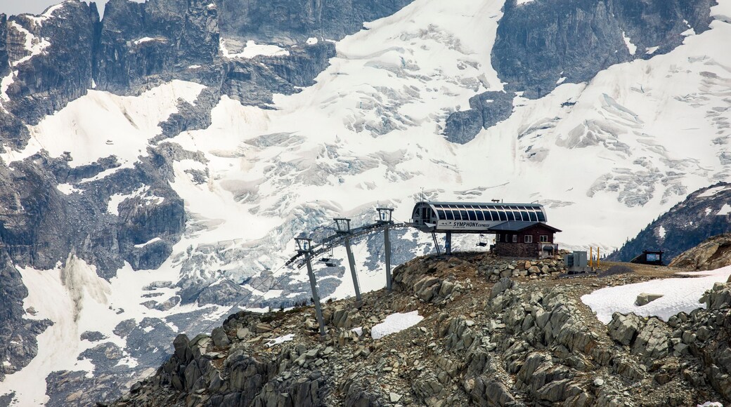 A chairlift comes to the top of a mountain backdropped by a glaciated peak behind in the Coast Mountains of British Columbia.