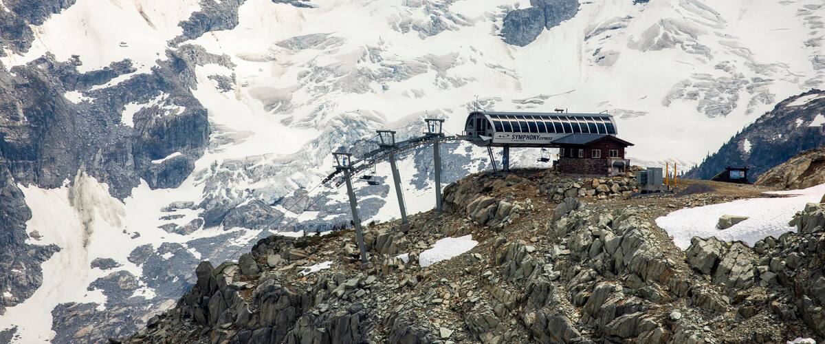 A chairlift comes to the top of a mountain backdropped by a glaciated peak behind in the Coast Mountains of British Columbia.