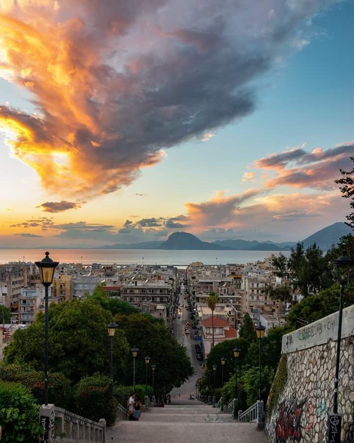 A cityscape with a view of the sea and mountains at sunset.