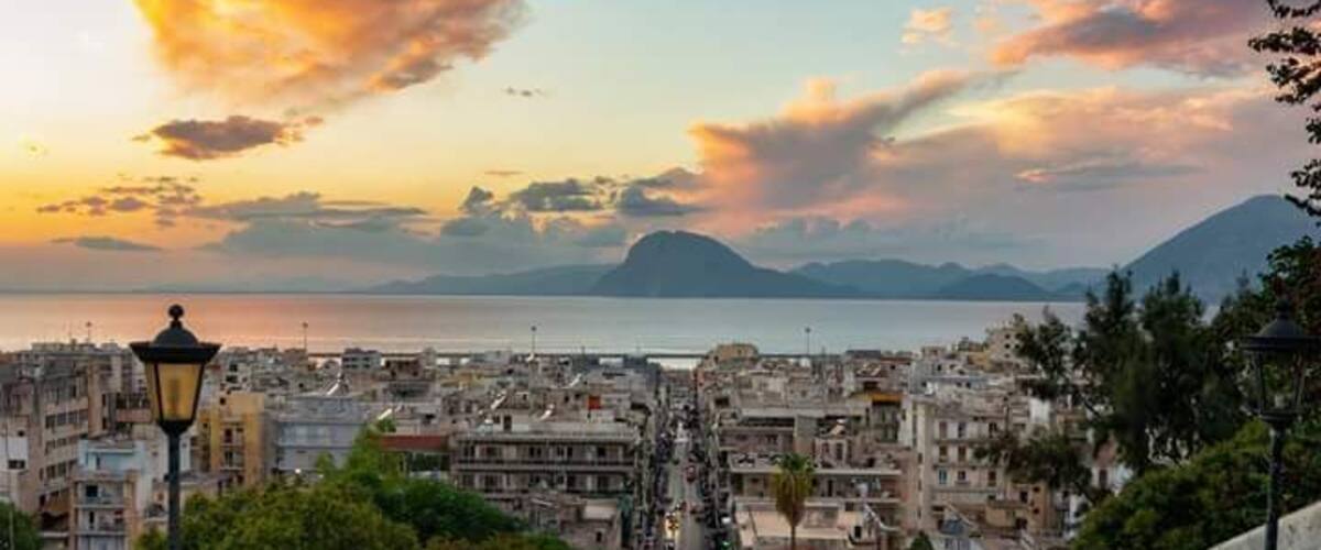 A cityscape with a view of the sea and mountains at sunset.