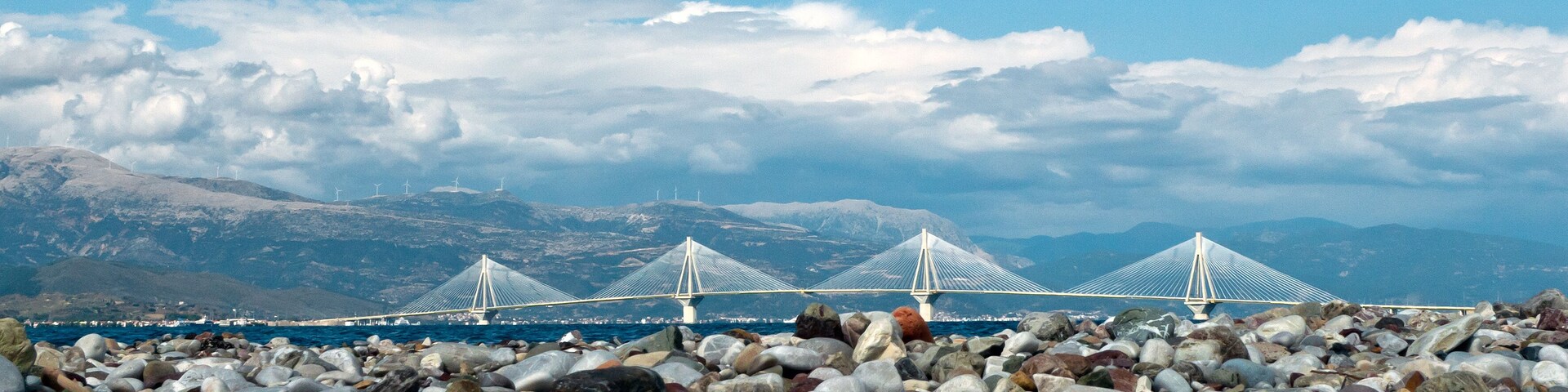 Un paisaje costero con un puente, piedras y montañas al fondo.