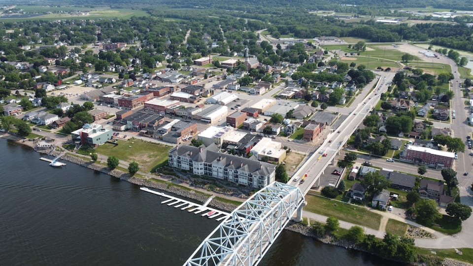An aerial view of a town with a prominent bridge over a river, surrounded by residential and commercial buildings.
