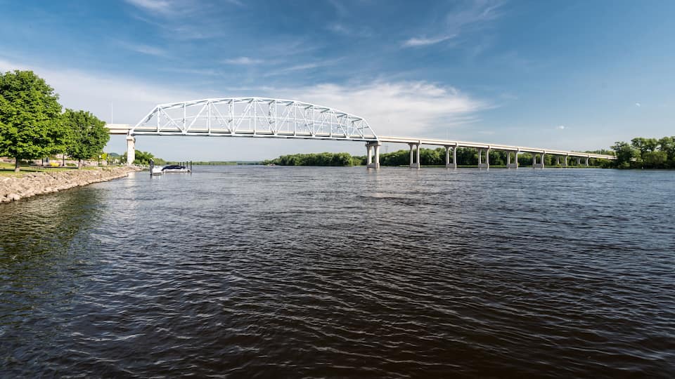 A white bridge over a river with trees and a clear sky.