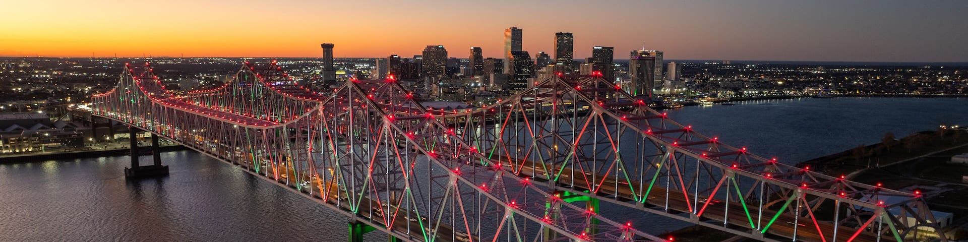 Aerial view of a majestic truss bridge adorned with vibrant red and green lights, spanning dark waters under a twilight sky, Freeport, Texas, United States.