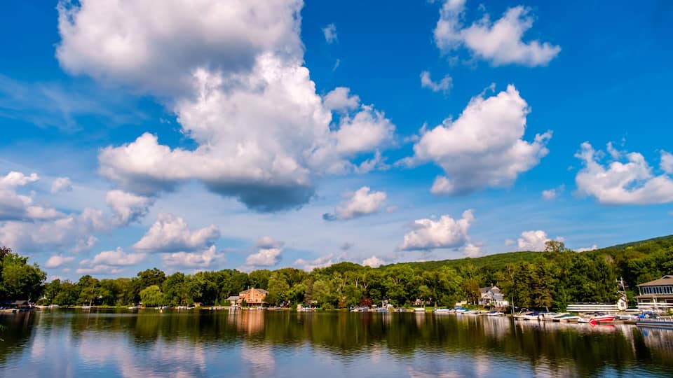 A lake with a clear sky, scattered clouds, and a forested hillside in the background.