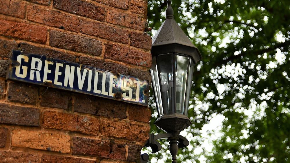 Un mur de briques avec une plaque de rue indiquant « RUE DE GREENVILLE » et un lampadaire noir.