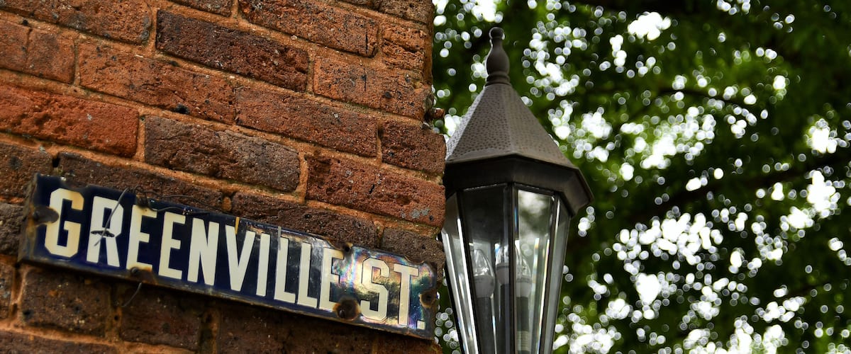 Urban setting, Greenville Street sign on the side of a brick building with a lantern and trees in the background
