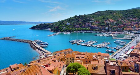 Une ville côtière dotée d’un port de plaisance, de bâtiments aux toits de tuiles rouges et d’une colline verdoyante.
