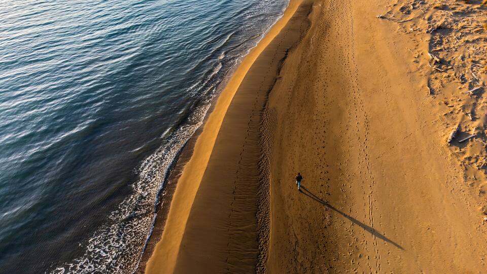 A sandy beach with gentle waves, a clear sky, and a person walking along the shore.