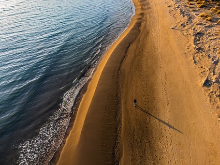 Une plage de sable fin aux vagues douces, un ciel dégagé et une personne qui se promène le long du rivage.