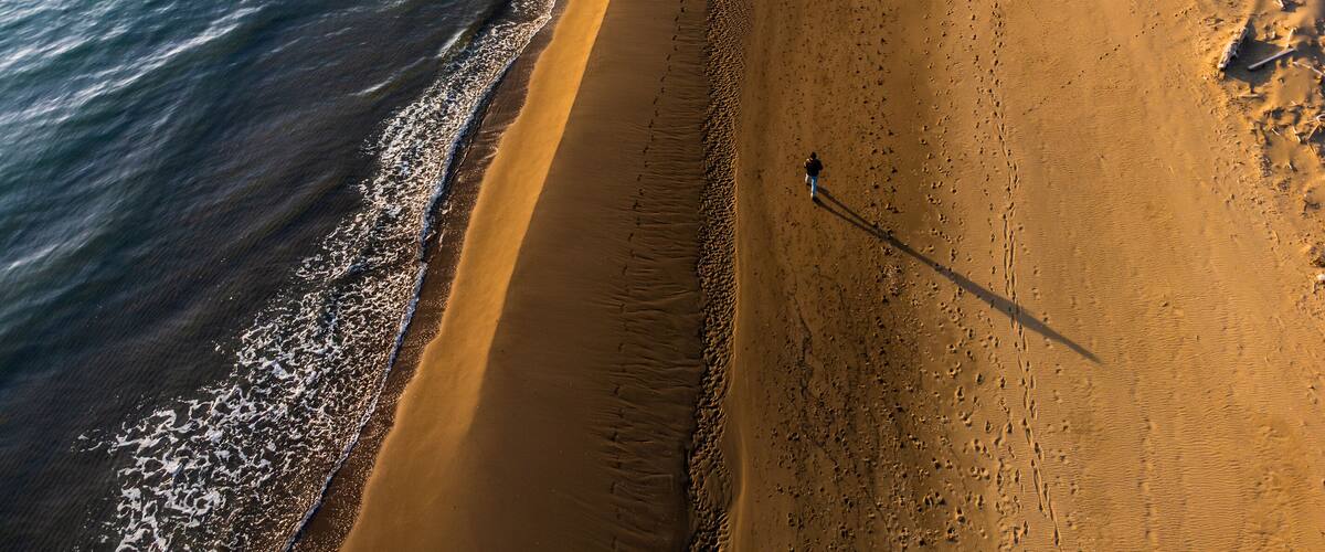 A sandy beach with gentle waves, a clear sky, and a person walking along the shore.