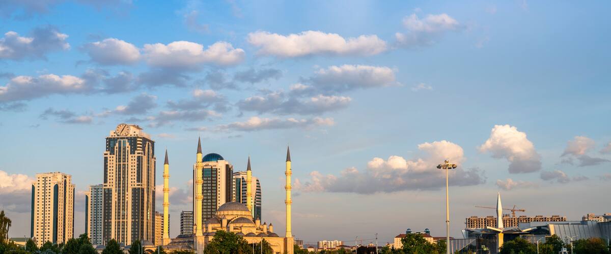 A city skyline with modern skyscrapers, a mosque with a minaret, and a construction crane in the distance.