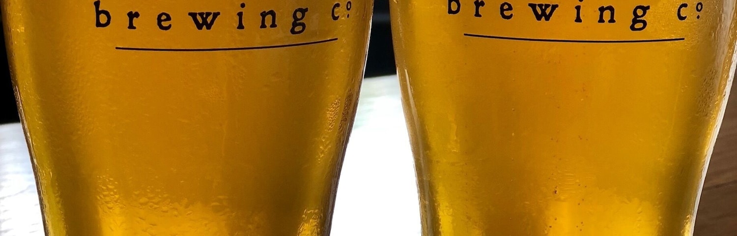 Duas cervejas com o rótulo 'GOSHEN brewing co' sobre uma mesa de madeira.